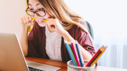 Woman looking at a computer, chewing pencil